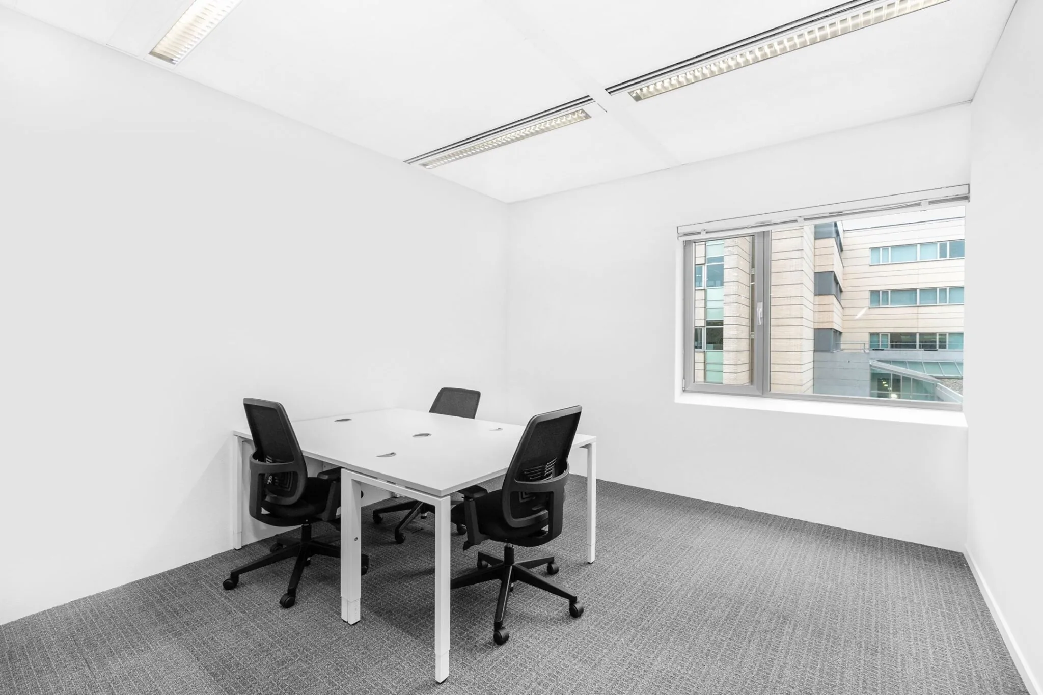 Kleine, moderne vergaderruimte aan de Papendorpseweg 95 met vier bureaustoelen, wit bureau en uitzicht op een kantoorgebouw.