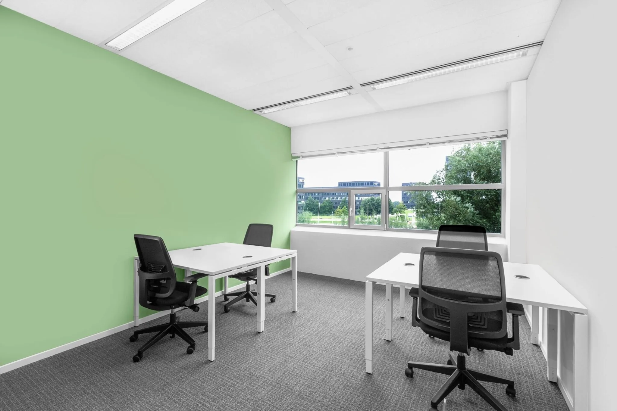 Moderne kantoorruimte aan de Papendorpseweg 95 met vier werkplekken, een mintgroene accentmuur en uitzicht op groen en kantoorgebouwen.