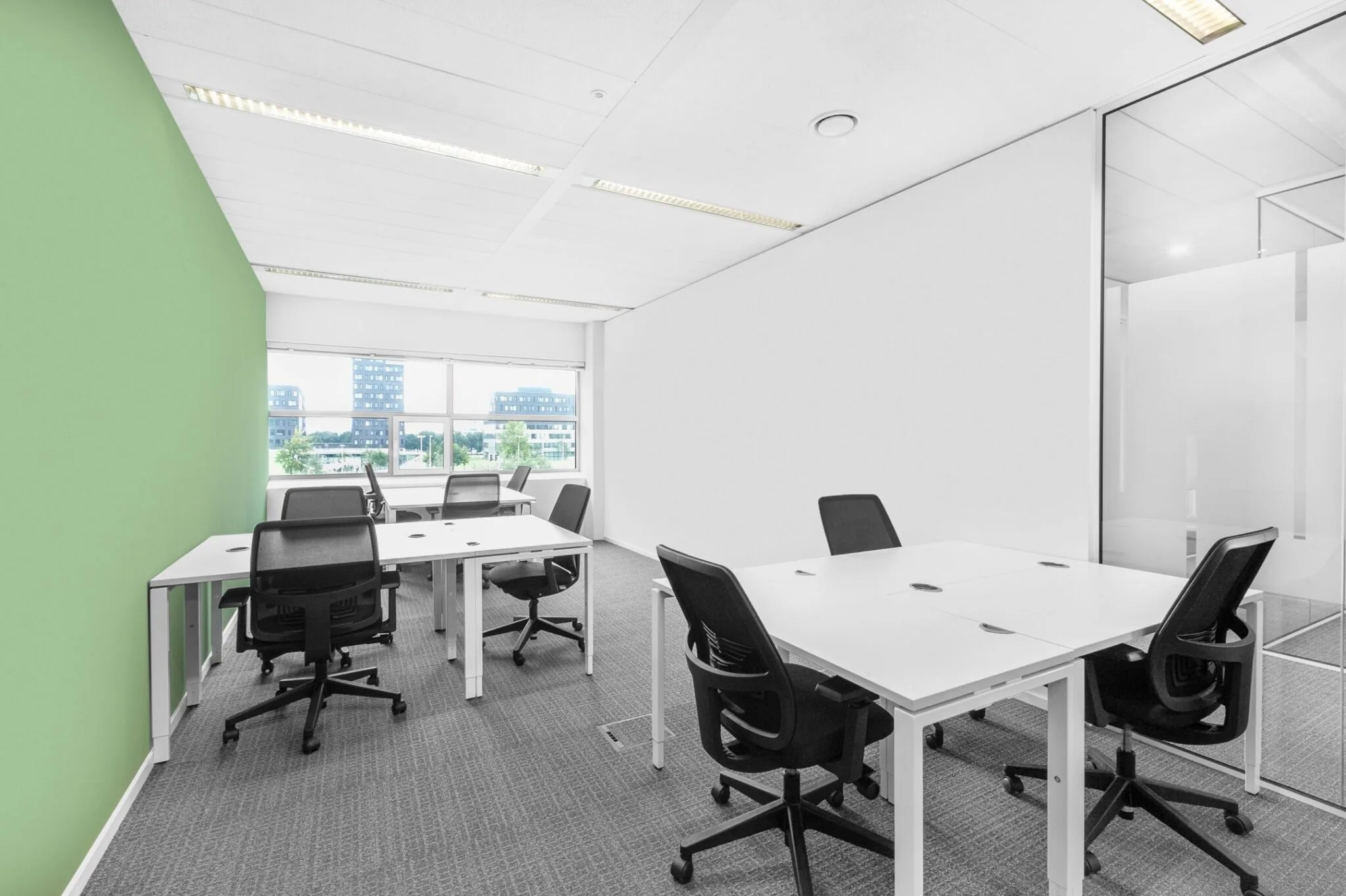 Moderne kantoorruimte aan de Papendorpseweg 95 met witte bureaus, zwarte bureaustoelen en een groene accentmuur.