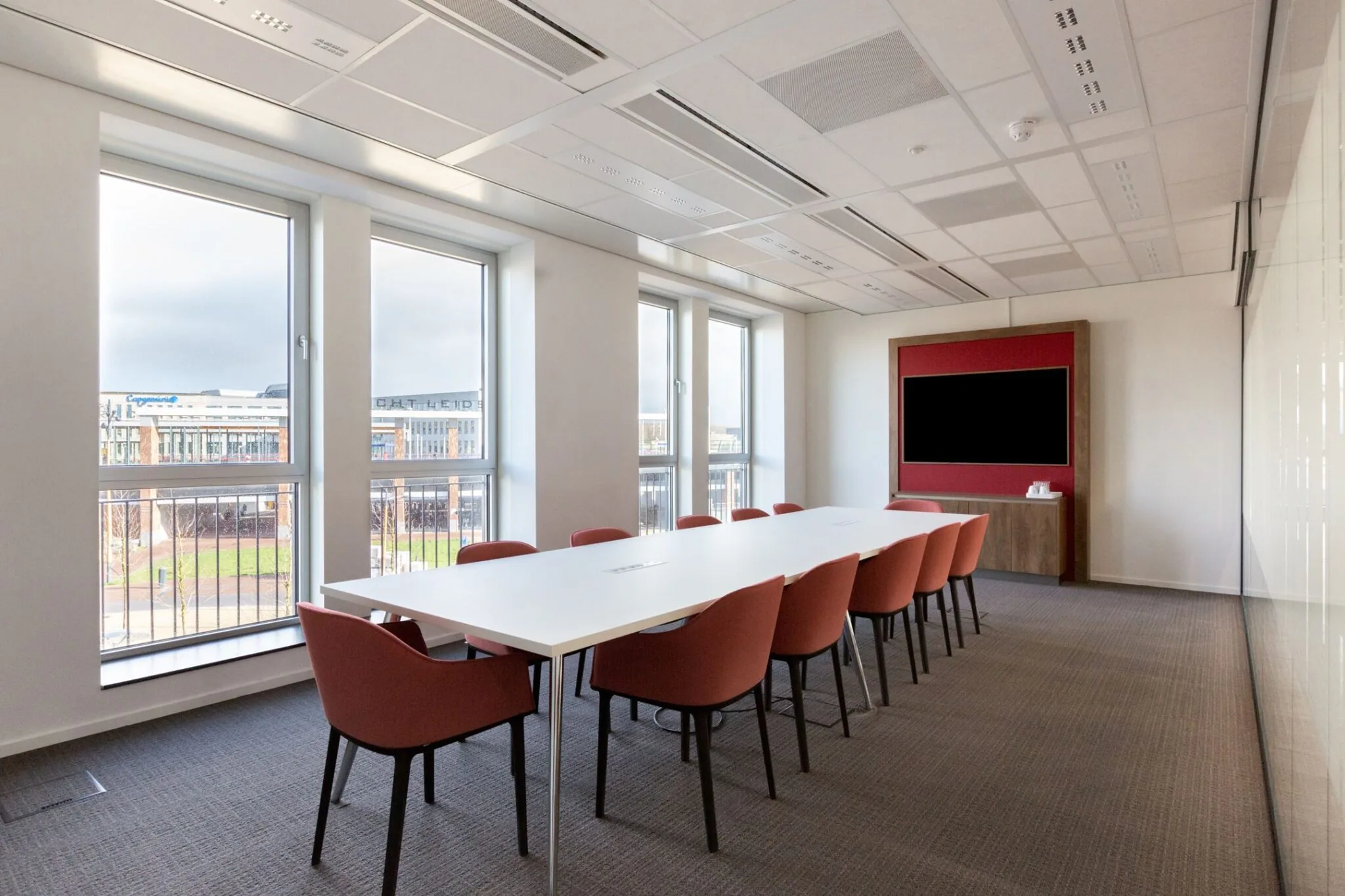 Vergaderruimte in Parijsboulevard 209 met lange tafel, rode stoelen en grote ramen met uitzicht op buiten.