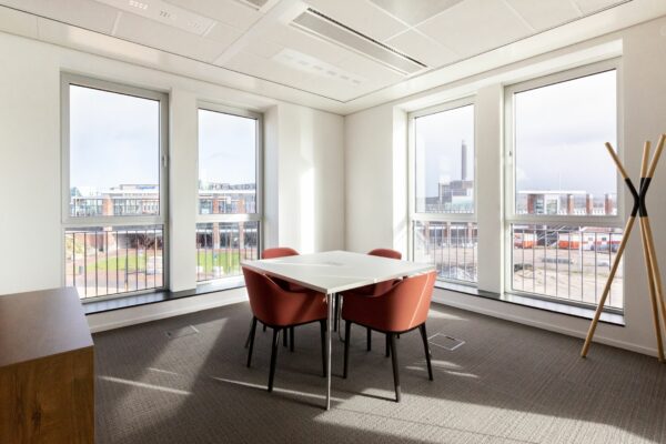 Vergaderruimte met vier rode stoelen rondom een witte tafel, gelegen aan de Parijsboulevard met uitzicht op het Stationsplein van Utrecht.