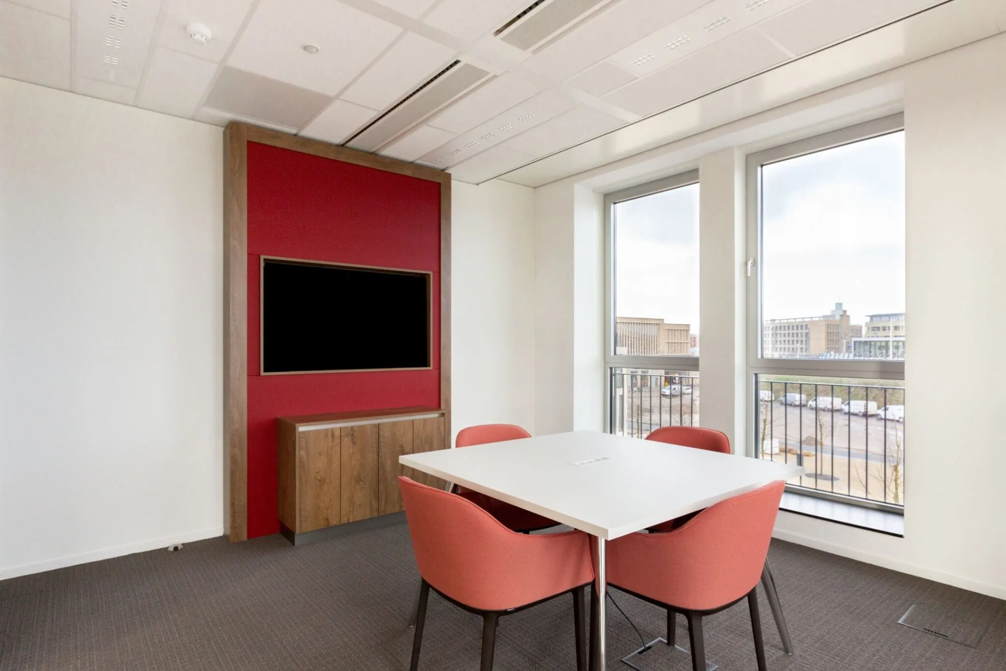 Vergaderruimte in Parijsboulevard 209 met witte tafel, rode stoelen, wandmeubel met televisie en uitzicht op moderne kantoorpanden.
