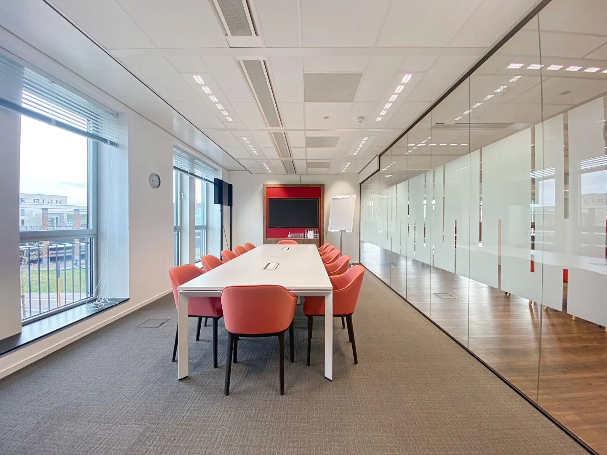 Moderne vergaderruimte aan de Parijsboulevard met een lange witte tafel, rode stoelen en glazen wanden.