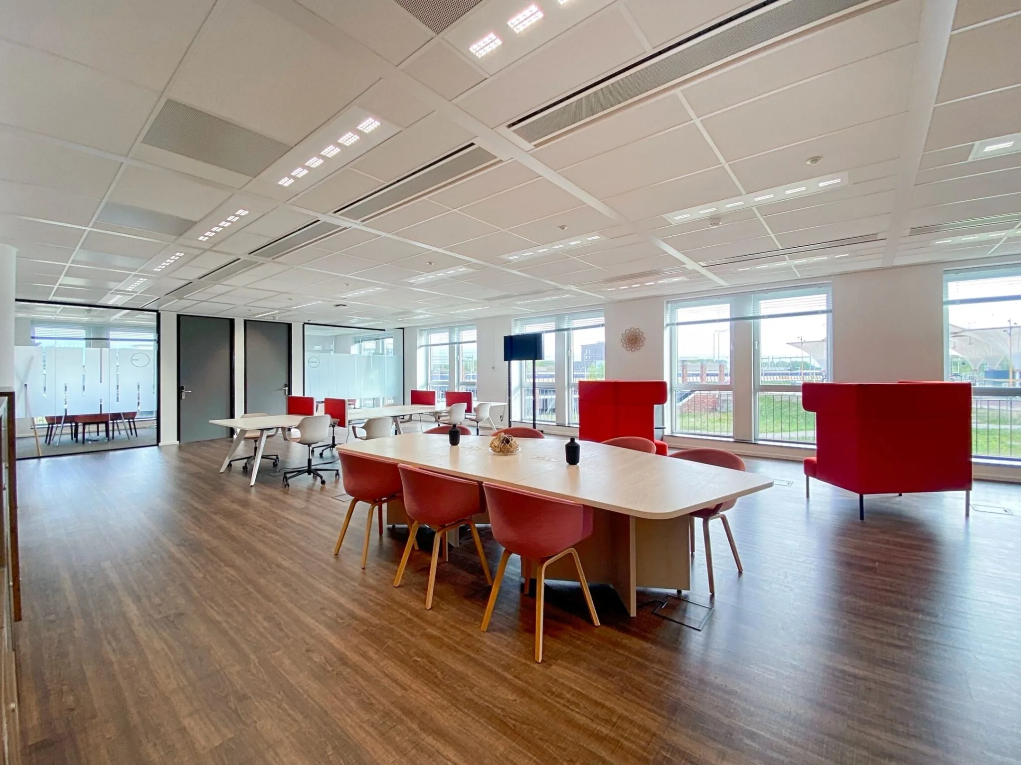 Moderne en lichte kantoorruimte aan de Parijsboulevard 209 met houten vloer, rode zitmeubels en grote ramen.