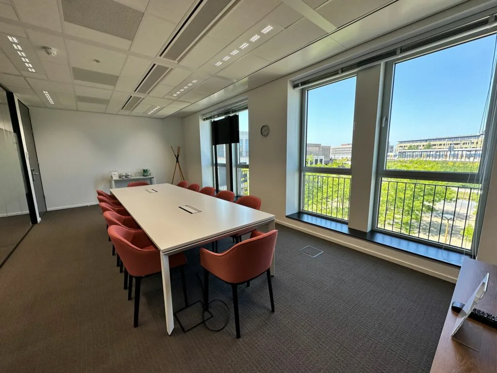Vergaderruimte met een lange tafel, rode stoelen en grote ramen met uitzicht op de Parijsboulevard.