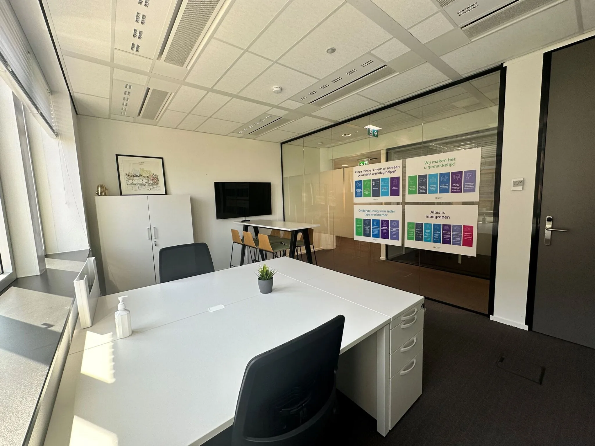 Modern kantoorinterieur op Parijsboulevard 209 met witte bureaus, vergadertafel, glazen wand en kleurrijke infoposters.