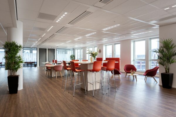 Moderne, licht ingerichte kantoorlounge op Parijsboulevard 209 met rode en roze stoelen, hoge tafels en grote ramen.