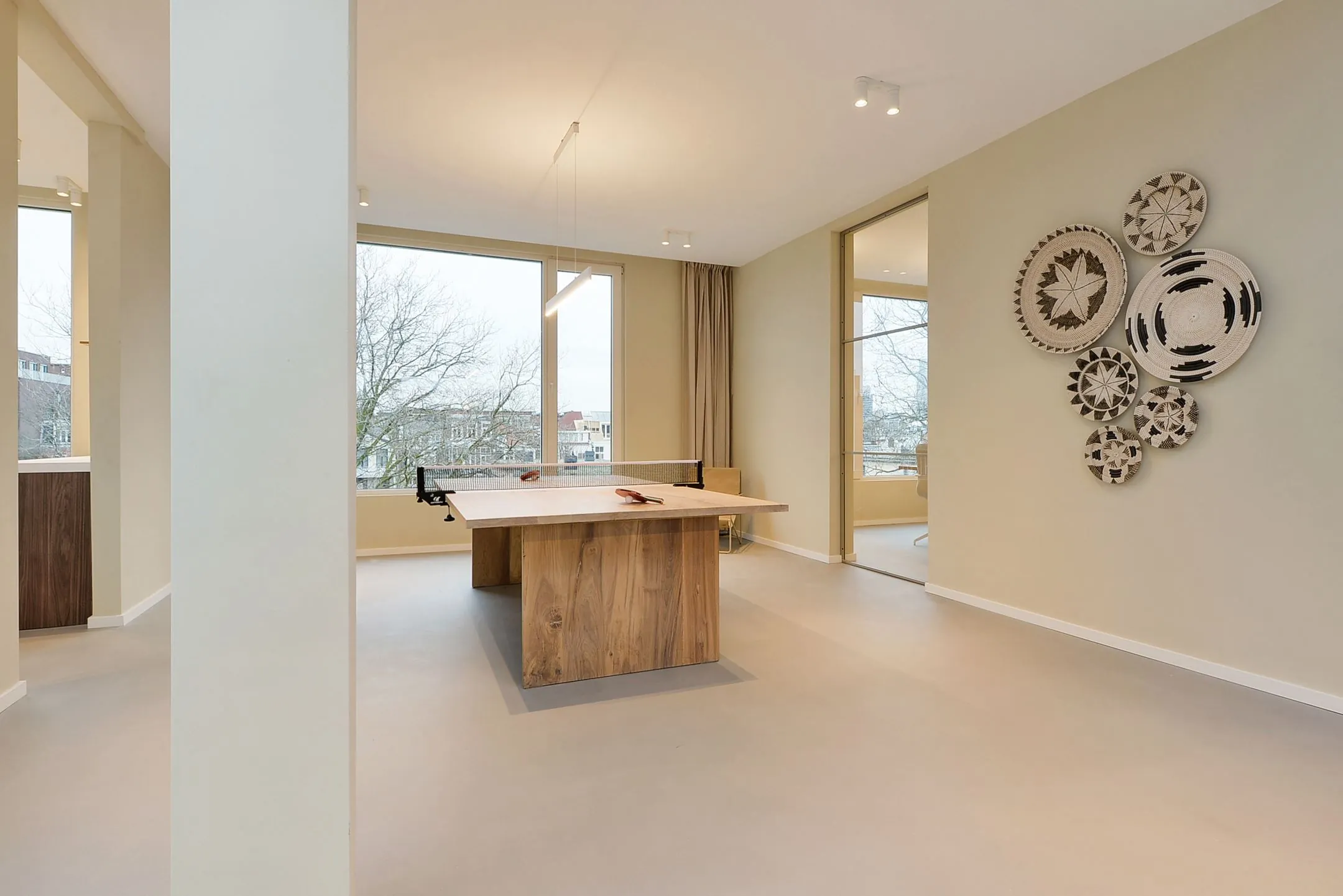Moderne ruimte met een houten tafeltennistafel, grote ramen en decoratieve wandkunst aan de muur bij Parkstraat 183.