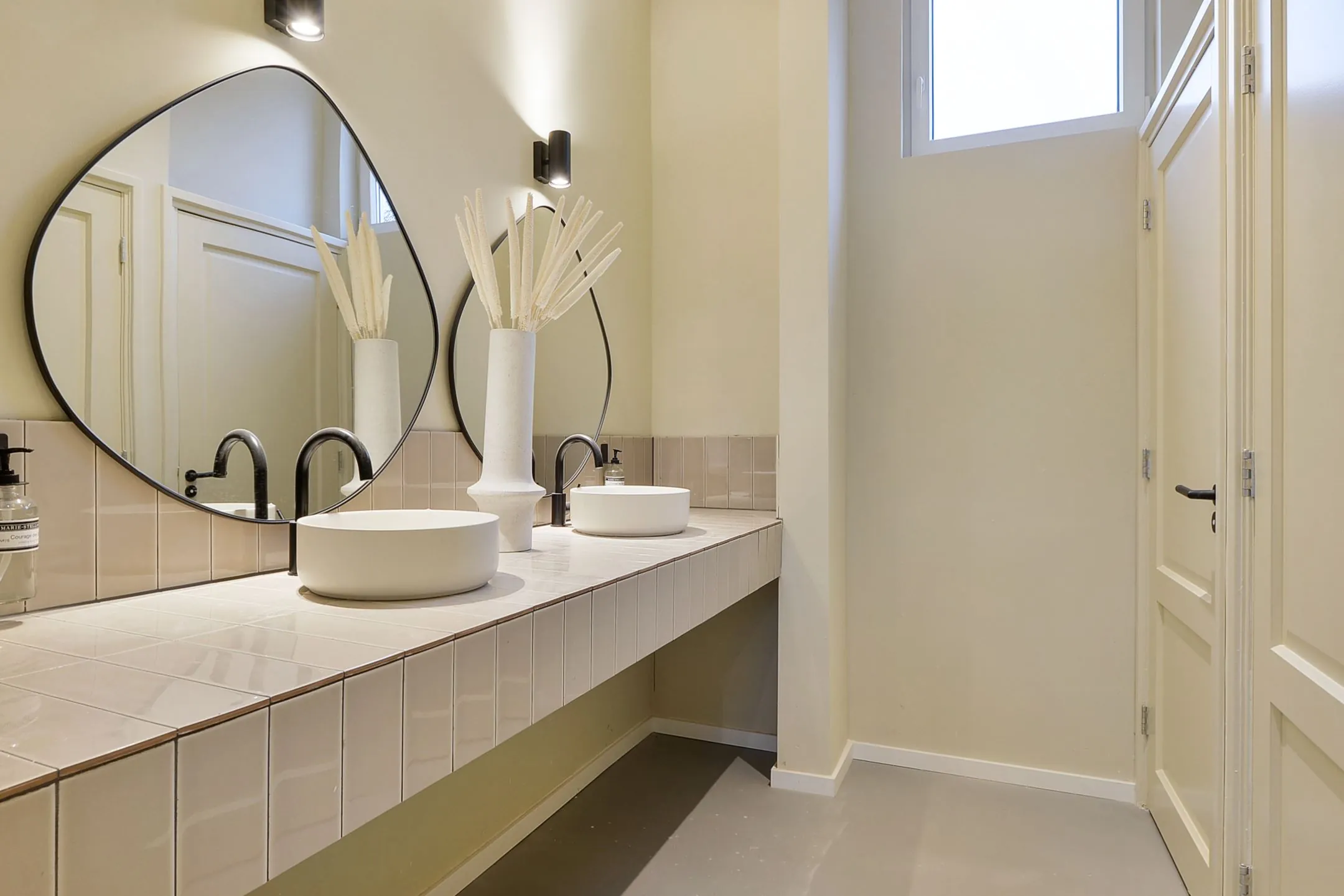 Moderne badkamer in Parkstraat 183 met twee ronde waskommen, asymmetrische spiegels en neutrale beige wandtegels.