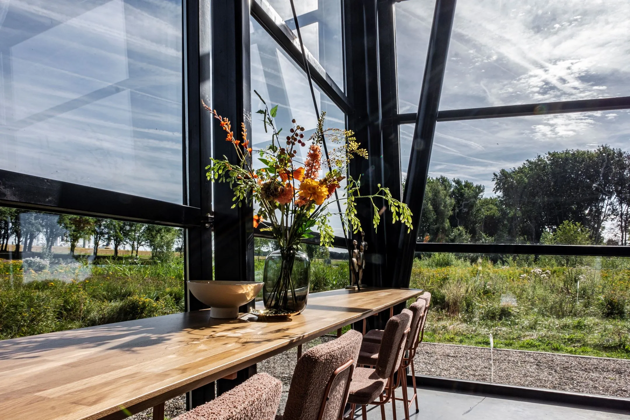 Lichte eetruimte met houten tafel, bloemenvaas en uitzicht op een groen landschap bij Plaatweg 15.