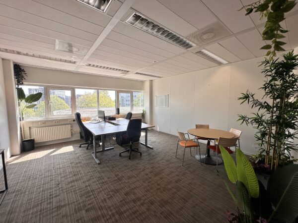 Licht en modern kantoor aan de Planetenweg 5 met werkplekken, ronde vergadertafel en veel groen.