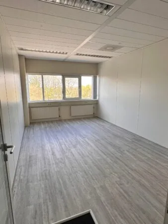 Lichte, lege kantoorruimte aan de Planetenweg 5 met grote ramen en grijze houten vloer.