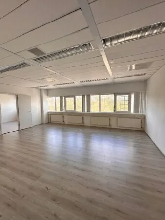 Lichte, lege kantoorruimte aan de Planetenweg 5 met grote ramen en laminaatvloer.