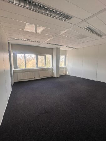 Leeg kantoor met donker tapijt, witte wanden en grote ramen bij Planetenweg 5.