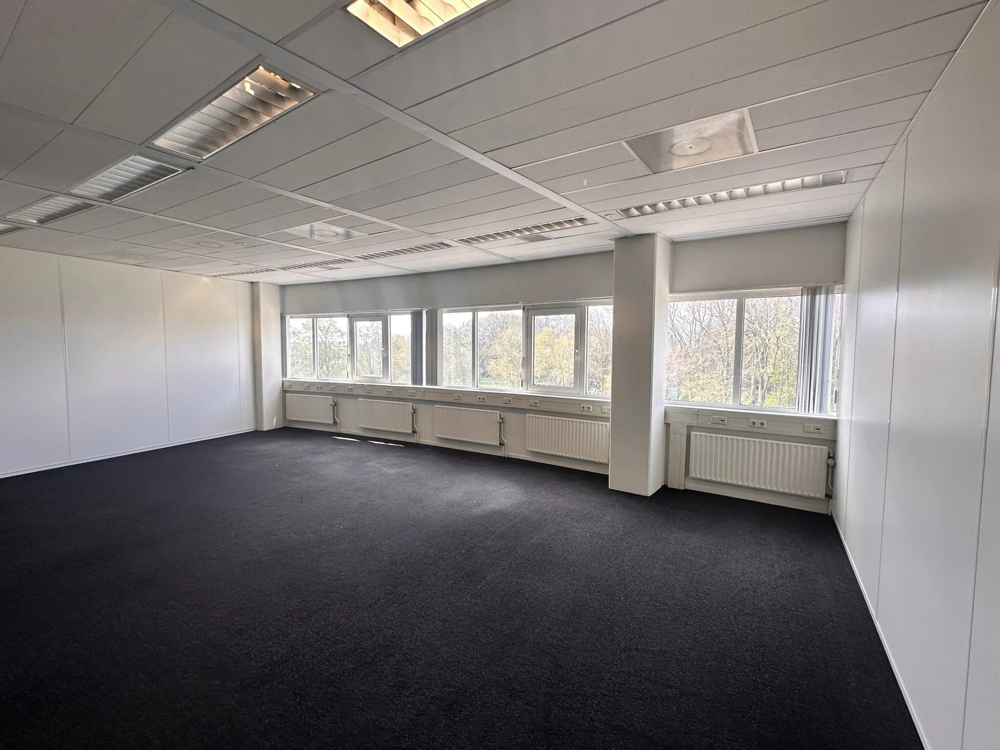Licht en ruim leeg kantoor met vloerbedekking en grote ramen aan de Planetenweg 5.