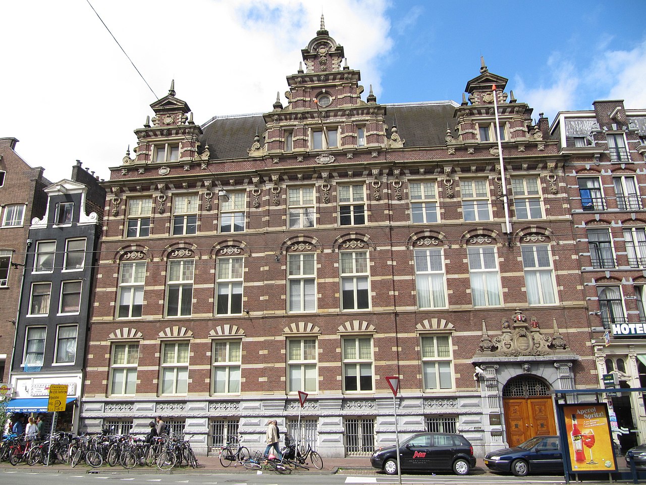 Gevel van een historisch pand aan de Nieuwezijds Voorburgwal 162 in Amsterdam, met rijke architectonische details en fietsen ervoor.