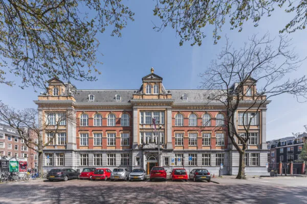 Monumentaal pand aan het Raamplein in Amsterdam met klassieke gevel, geparkeerde auto's en bomen op de voorgrond.