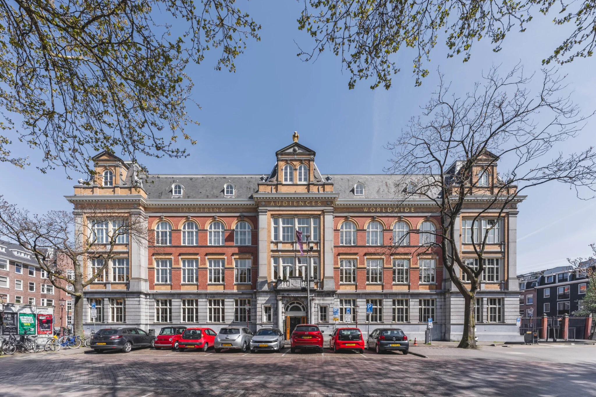 Monumentaal pand aan het Raamplein in Amsterdam met klassieke gevel, geparkeerde auto's en bomen op de voorgrond.