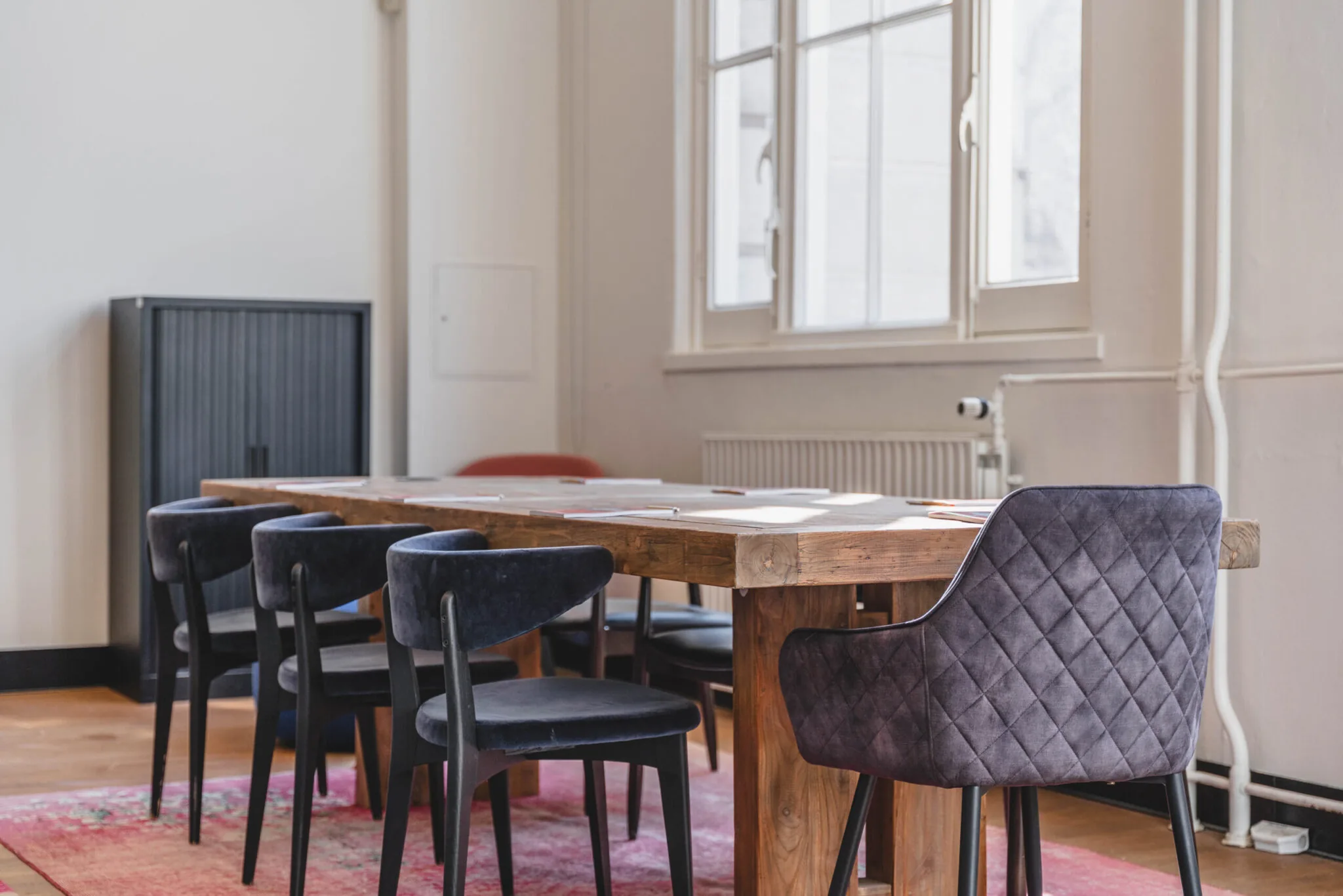 Vergaderruimte op Raamplein met een houten tafel, donkerblauwe stoelen en een groot raam dat natuurlijk licht binnenlaat.