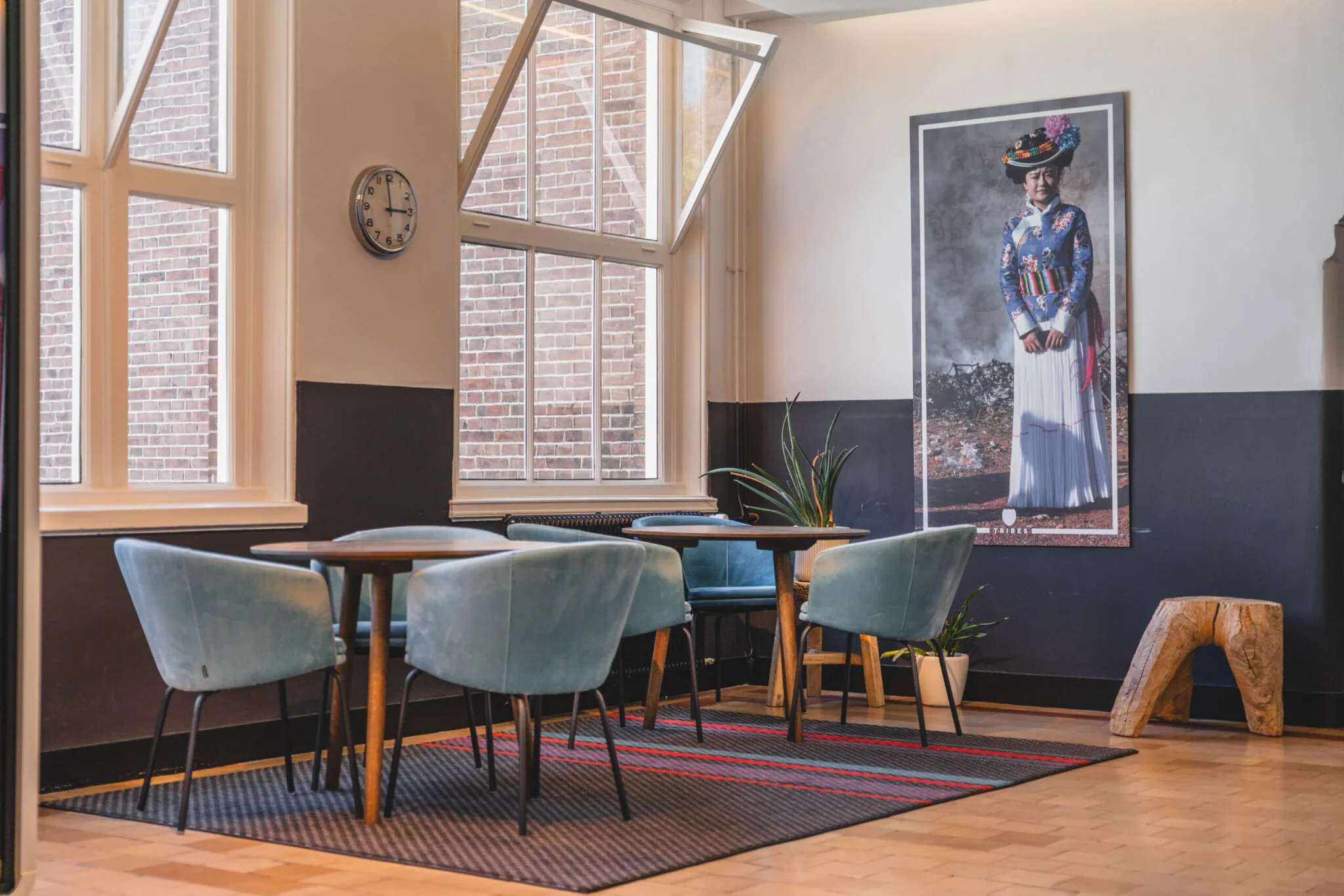 Stijlvol ingerichte zithoek op Raamplein 1 met blauwe stoelen, grote ramen en een kleurrijk portret aan de muur.