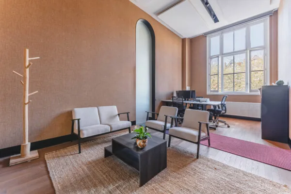 Stijlvol ingericht kantoor aan het Raamplein met een zithoek, bureau en grote ramen die uitzicht bieden op bomen.