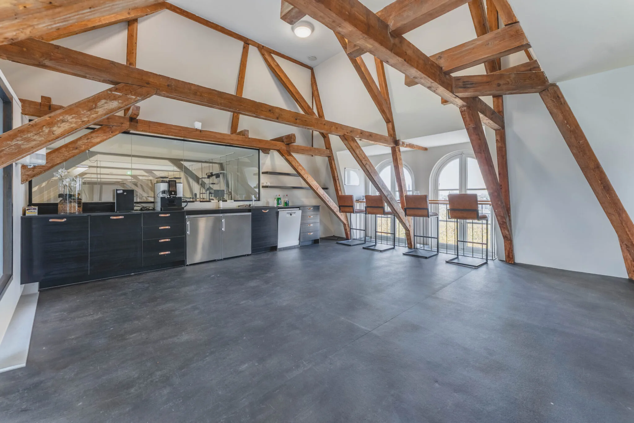 Moderne kitchenette met zitgedeelte in een open ruimte met houten balken en boograampjes aan het Raamplein 1-31.