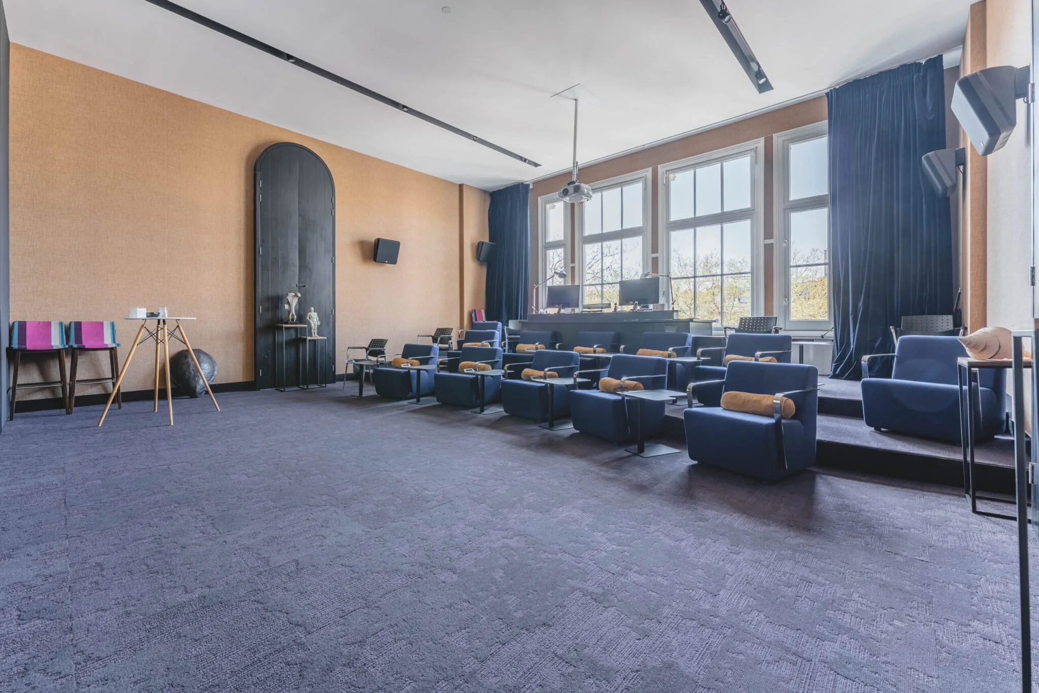 Moderne vergaderruimte in Raamplein 1-33 met comfortabele blauwe stoelen, groot raam en presentatieruimte.