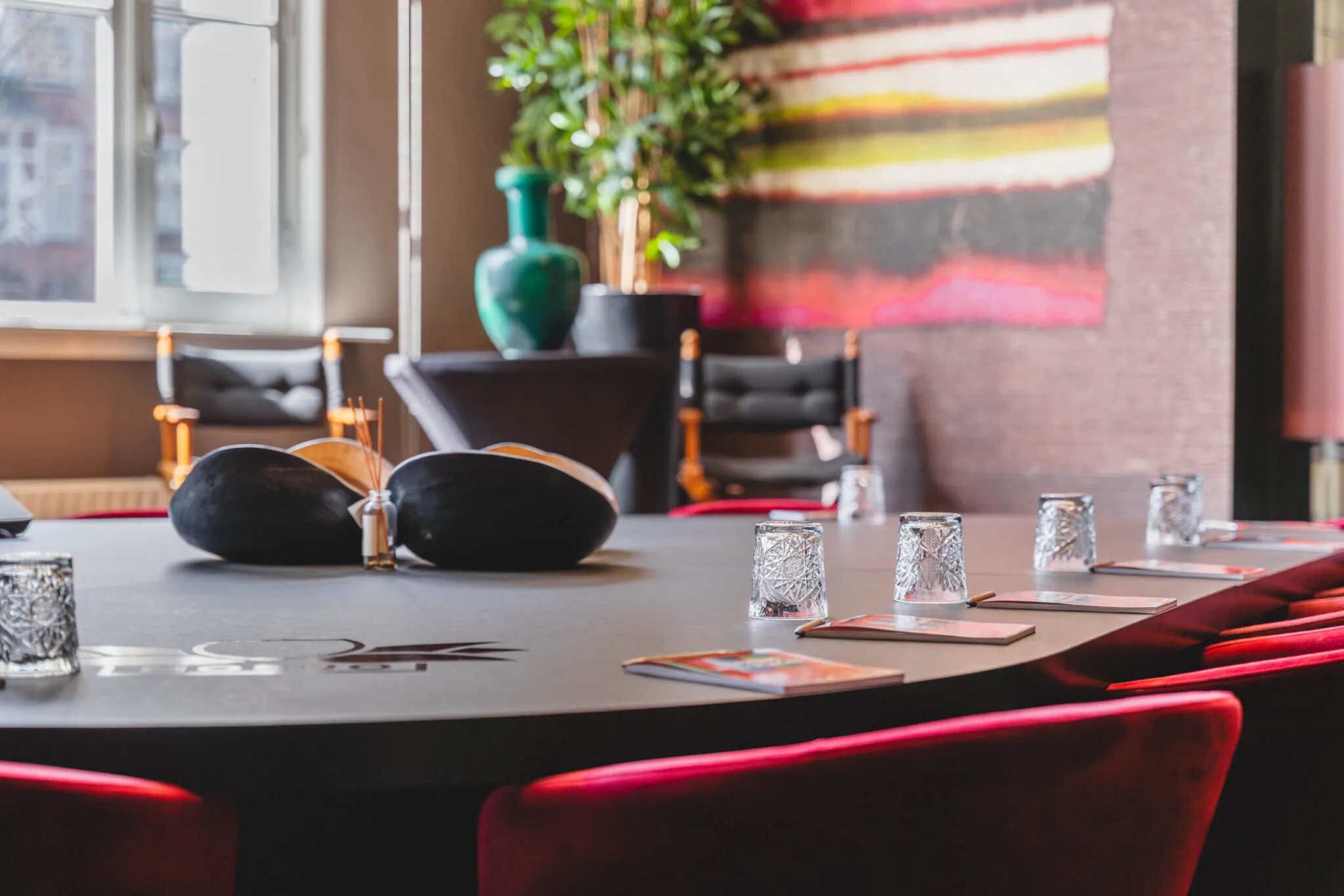 Vergaderruimte op Raamplein met ovale tafel, rode stoelen, glazen bekers en kleurrijke wanddecoratie.