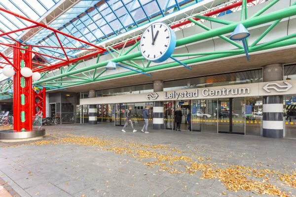 Voorgevel van treinstation Lelystad Centrum met opvallende kleurrijke staalconstructie en grote klok.