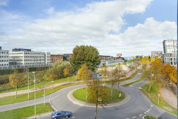 Rondweg met rotonde bij Ravelijn 1 in Helmond, omringd door herfstkleurige bomen en moderne kantoorgebouwen.
