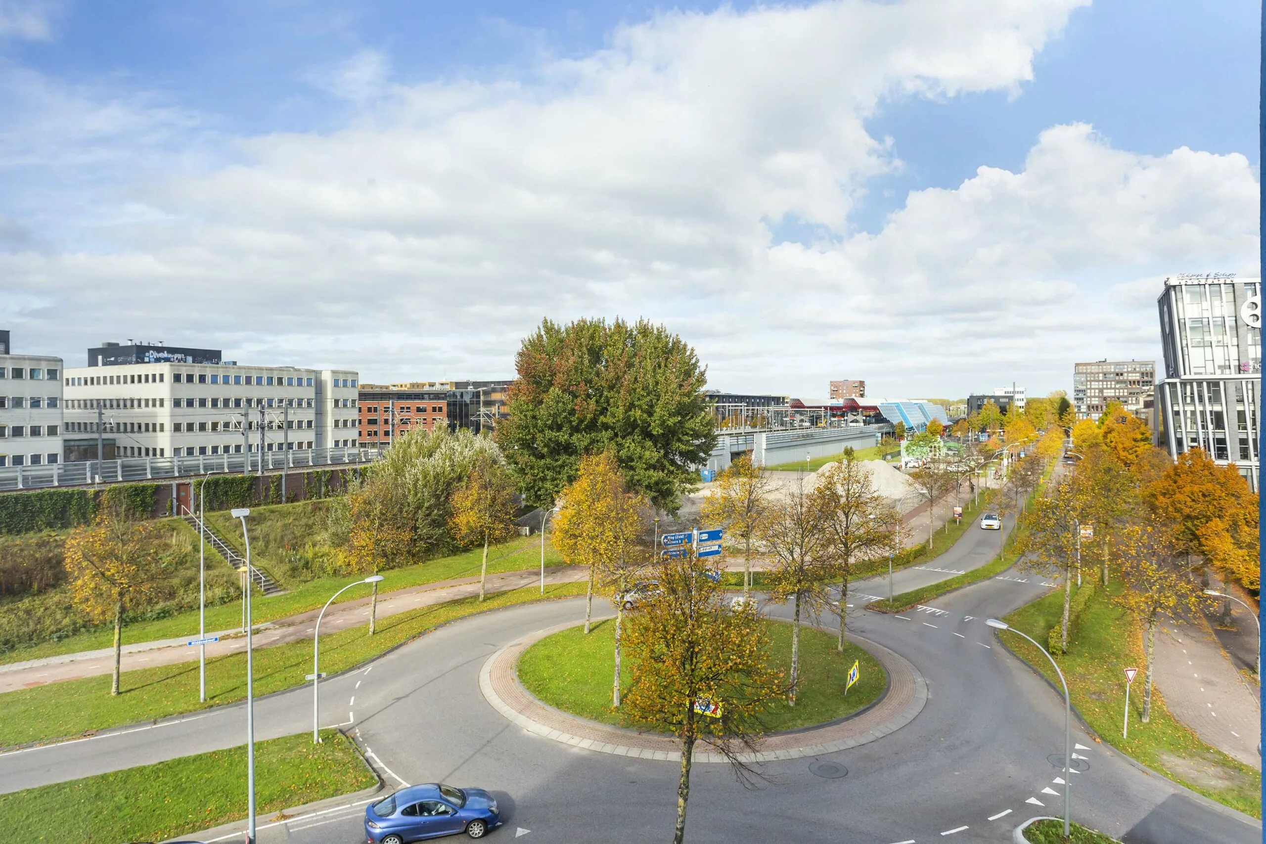 Rondweg met rotonde bij Ravelijn 1 in Helmond, omringd door herfstkleurige bomen en moderne kantoorgebouwen.