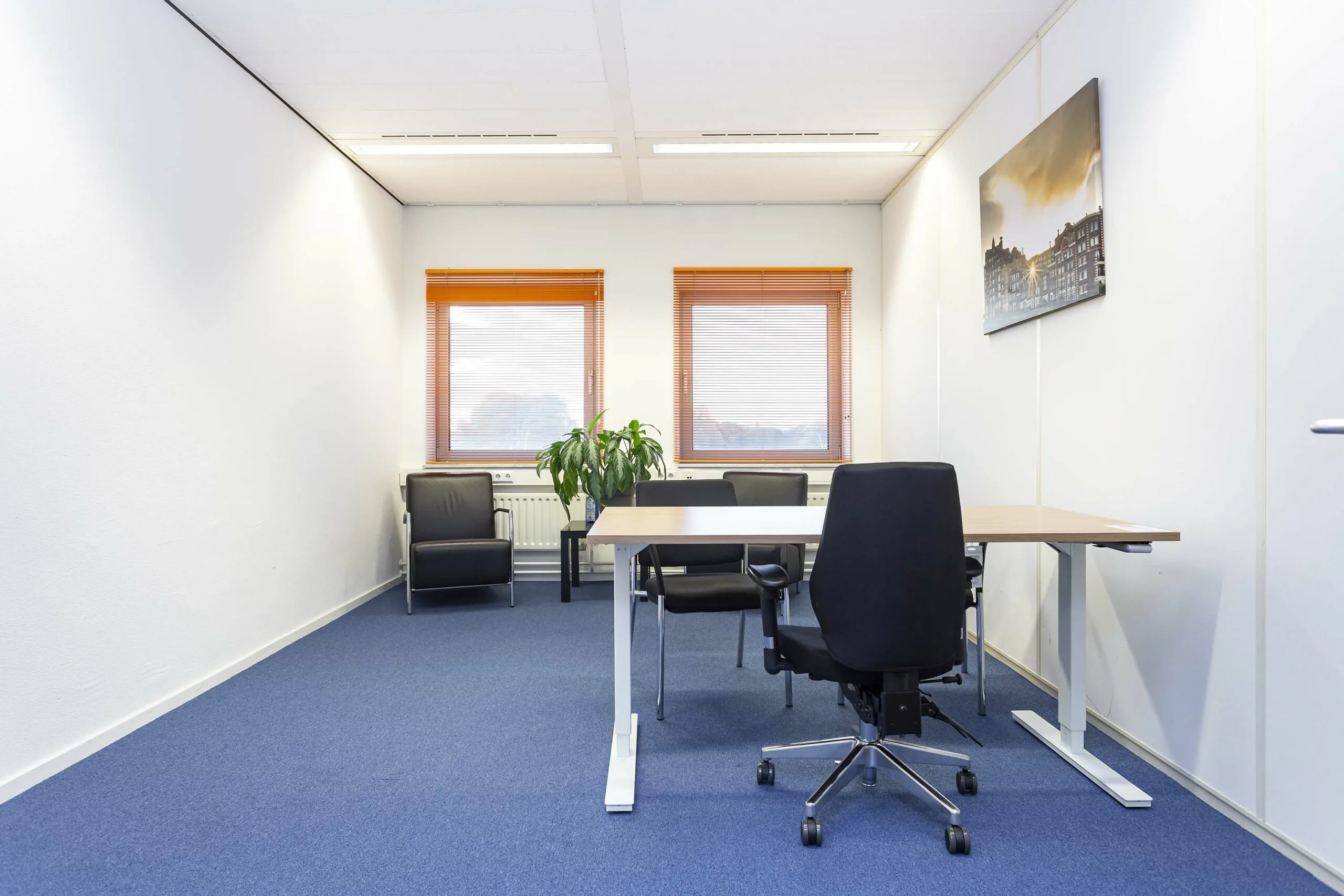Modern ingerichte kantoorruimte in Ravelijn 1 met bureaus, stoelen, kamerplanten en twee ramen met oranje jaloezieën.