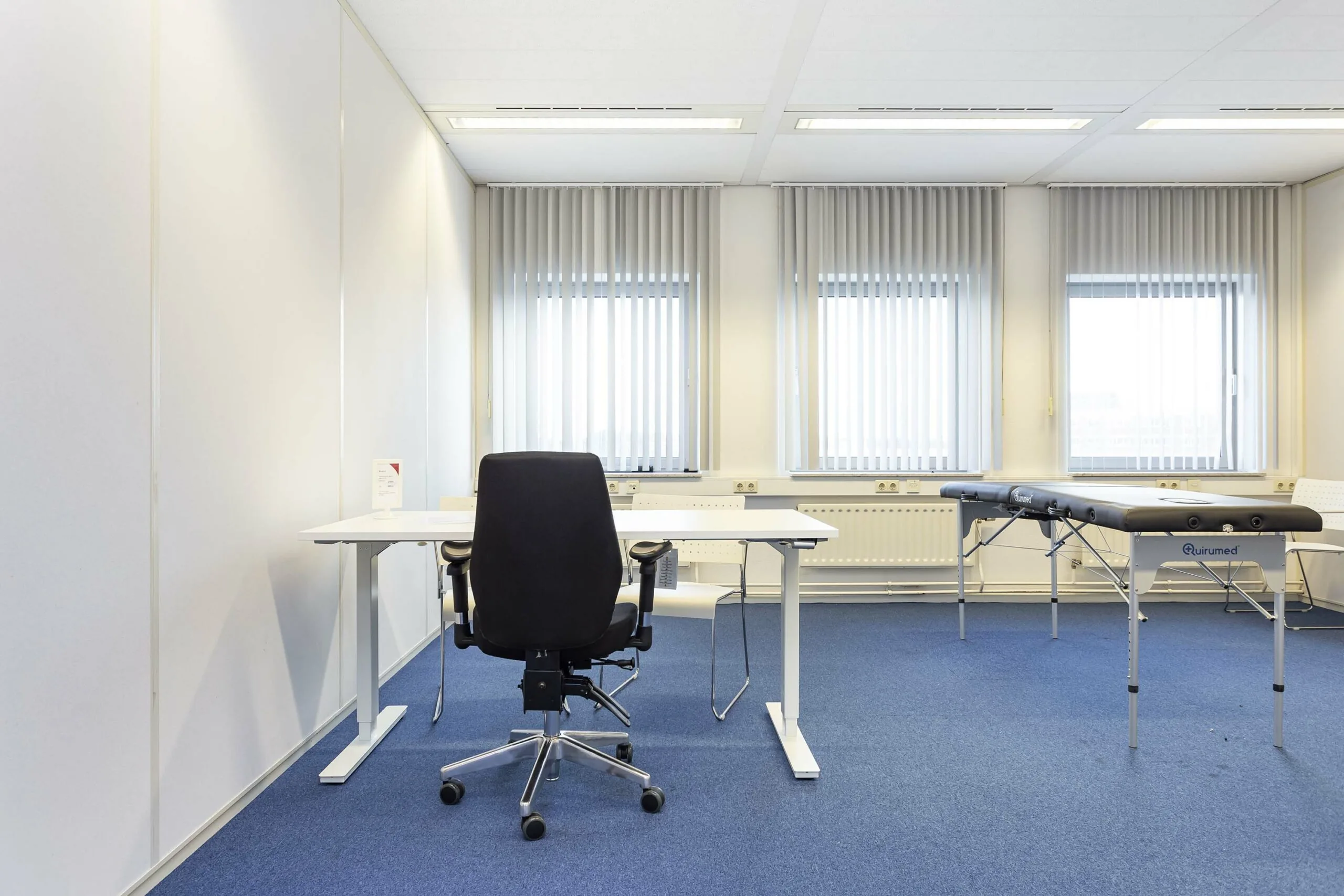 Lichte, moderne behandelkamer in Ravelijn 1 met bureau, bureaustoel en behandeltafel.