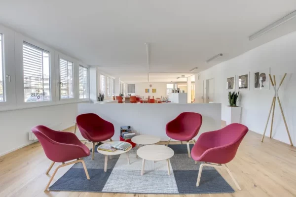 Moderne wachtruimte in Regus Bremen TechPark met rode designstoelen en ronde salontafels.
