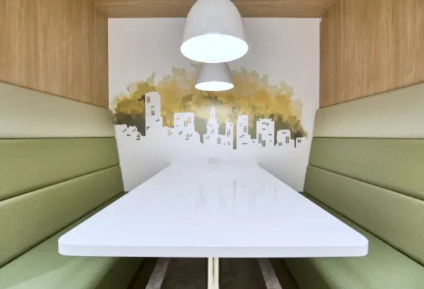 Kleine zithoek in Regus KDX 5709 Nagoya Ekimae met groene banken, witte tafel en muurschildering van een skyline.