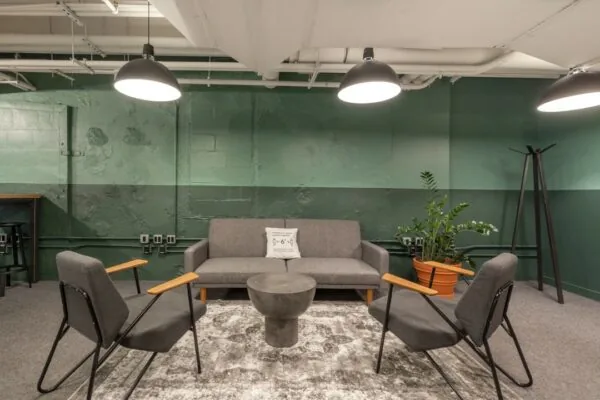Moderne wachtruimte met grijze zitmeubelen, een ronde betonnen tafel en een groene muur in een kantoor op Rotterdam Airportplein 22.