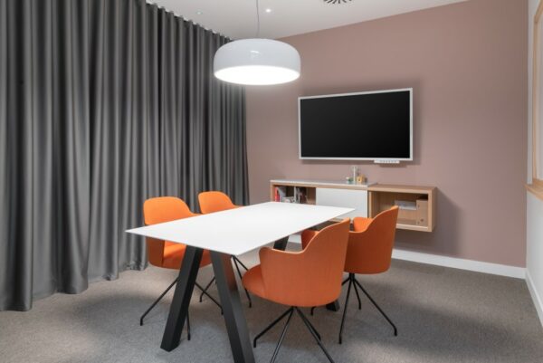 Vergaderruimte op Rotterdam Airportplein 22 met witte tafel, vier oranje stoelen, flatscreen en moderne verlichting.