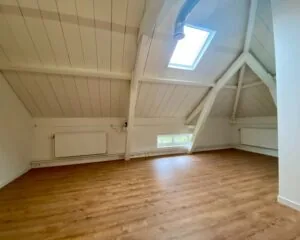 Lichte zolderruimte aan de Utrechtseweg 82 met houten vloer, witgeschilderde balken en dakraam.