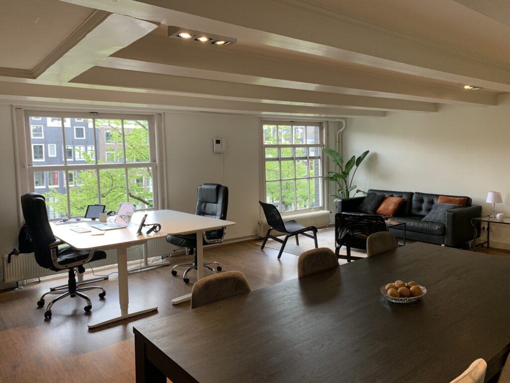 Moderne kantoorruimte met bureau, vergadertafel, zithoek en grote ramen met uitzicht op de stad.