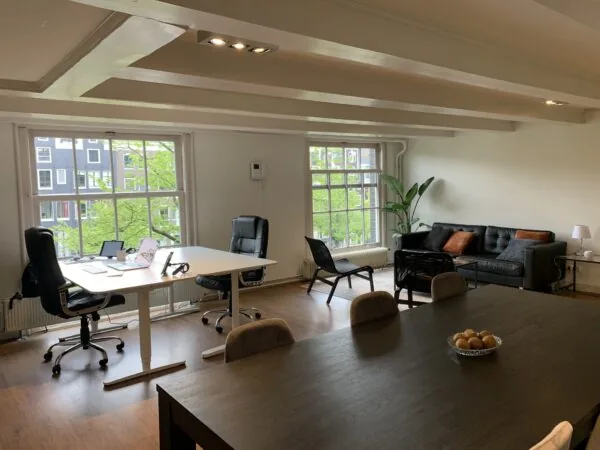 Moderne kantoorruimte met bureau, vergadertafel, zithoek en grote ramen met uitzicht op de stad.