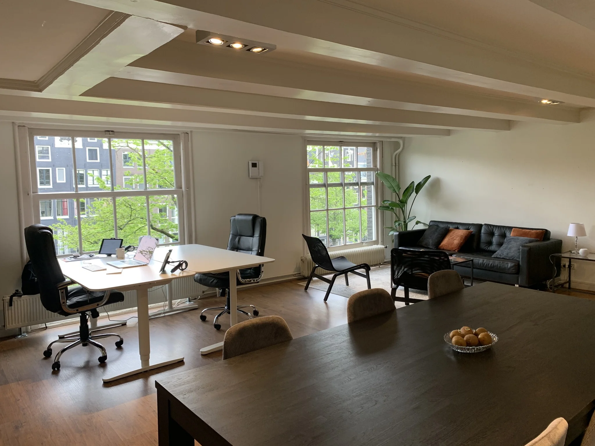 Moderne kantoorruimte met bureau, vergadertafel, zithoek en grote ramen met uitzicht op de stad.