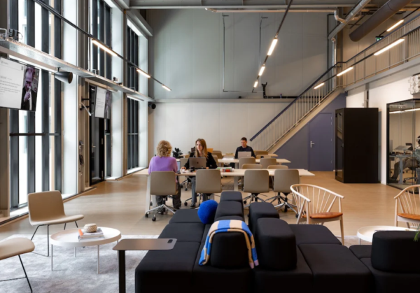 Een moderne kantoorruimte met grote ramen, waarin mensen aan tafels werken.