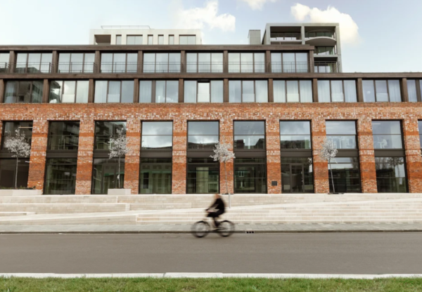 Een modern bakstenen gebouw met grote ramen en een fietser die er langs rijdt.