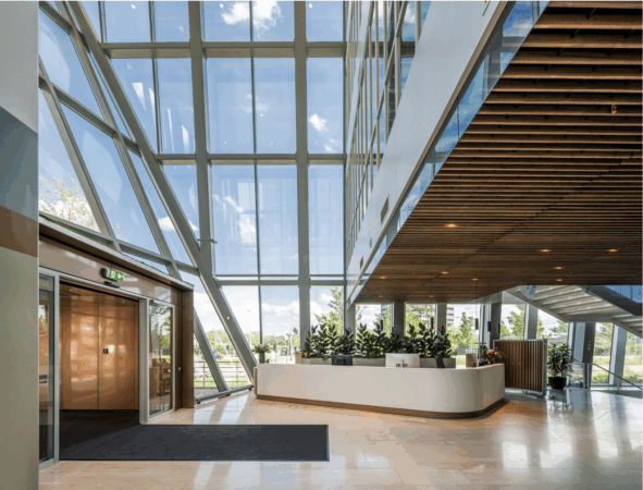 Moderne, lichte kantoorlobby met glazen gevel, houten plafond en een witte receptiebalie.