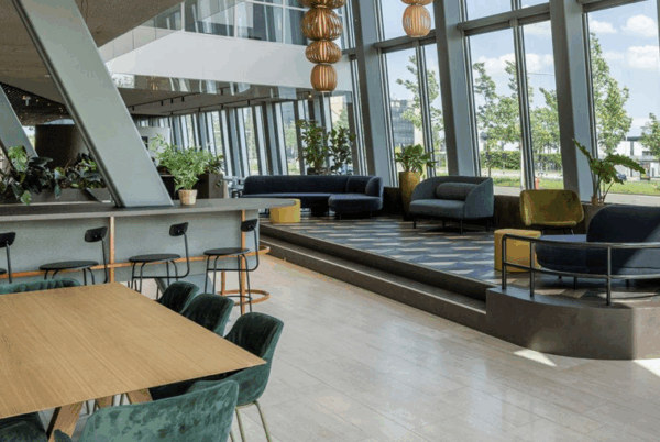 Moderne en lichte kantoorlounge met zithoeken, hoge ramen en groenaccenten.