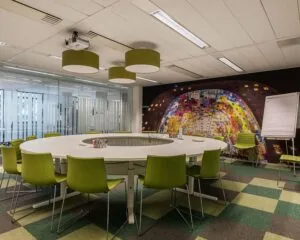 Moderne vergaderruimte met ronde tafel, groene stoelen en een kleurrijke muurfoto van de Markthal in Rotterdam.