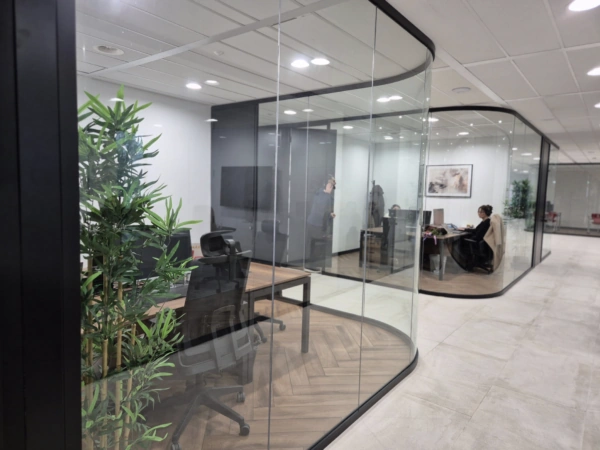 Moderne kantoorruimte met glazen wanden, waar mensen aan het werk zijn in afzonderlijke vergaderruimtes.