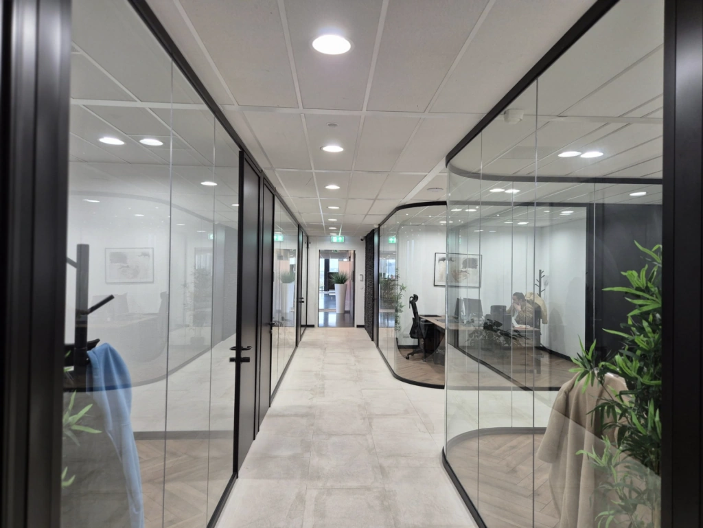 Een moderne kantoorruimte met glazen wanden, waarin een medewerker achter een bureau werkt.