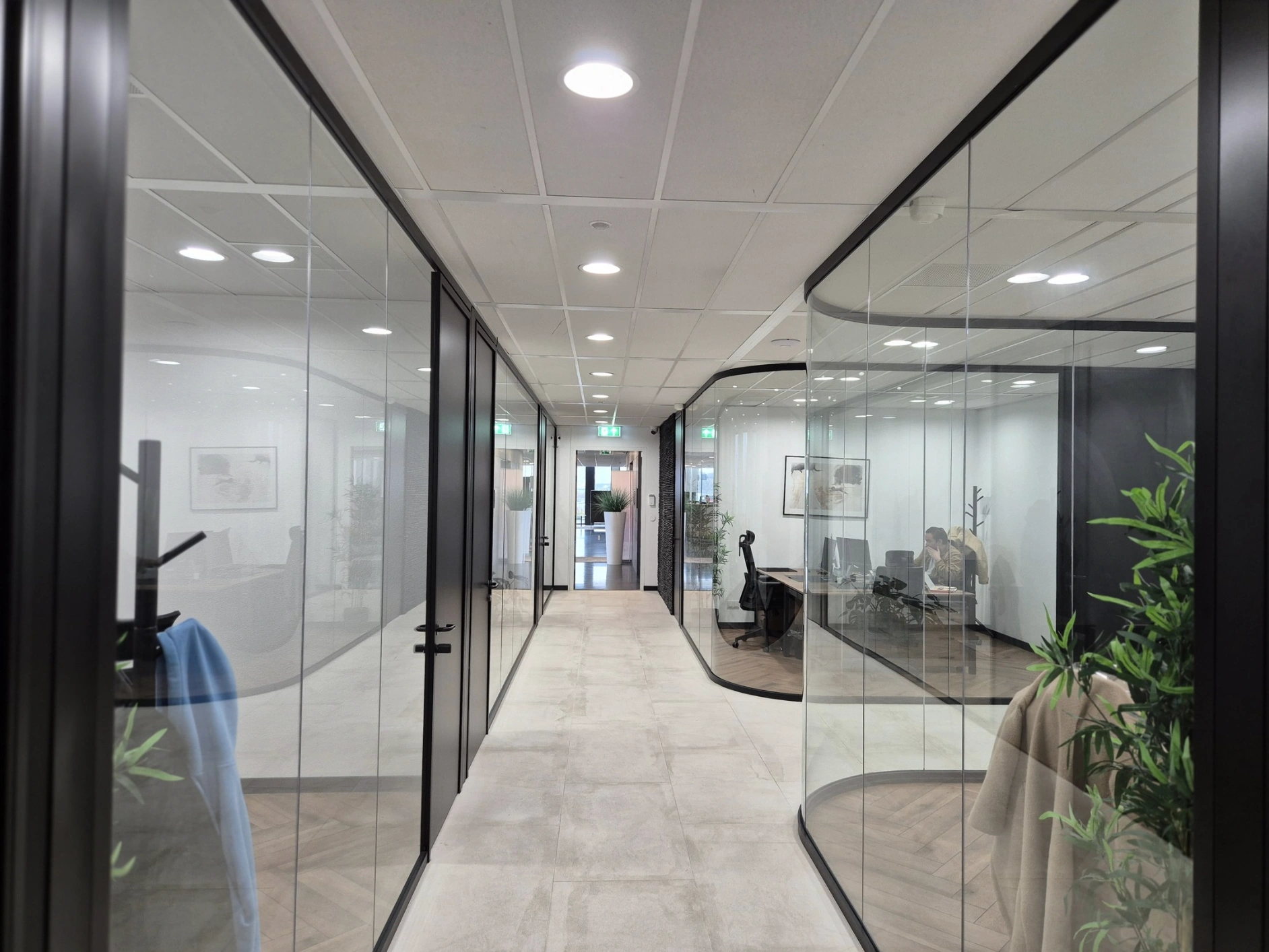 Een moderne kantoorruimte met glazen wanden, waarin een medewerker achter een bureau werkt.