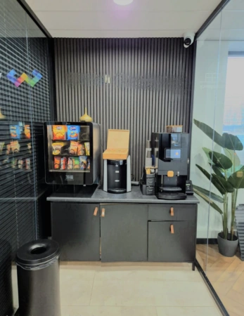 Koffie- en snackhoek met automaten, bekerdispenser en prullenbak in een modern kantoor.